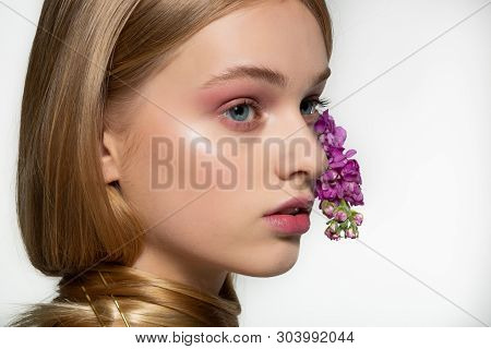 Close Up Portrait Of Young Girl With Blue Eyes, Bright Makeup, Neck Wrapped In Hair, Purple Flowers 