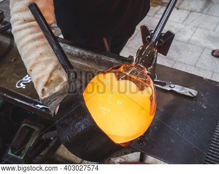 Art Glassblower Use Wet Wooden Form For Shaping The Red Melted Glass On The End Of Glassblowing Pipe