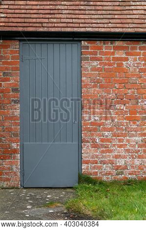 A Wooden Grey Painted Door In A Red Brick Building With A Tiled Roof. Variety Of Textures And Colour