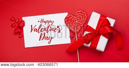 Valentines day greeting card. Gift boxes and heart candy sweets over red background. Top view flat lay