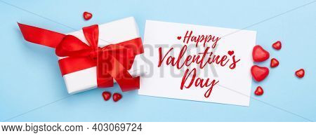 Valentines day greeting card. Gift box and heart candy sweets over blue background. Top view flat lay