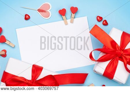 Valentines day greeting card template. Gift boxes, heart decor and candy sweets over blue background. Top view flat lay with copy space