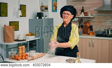 Happy Old Baker Woman Claping Hands With Flour At Camera. Professional Cook Claps And Powder Fly, Re