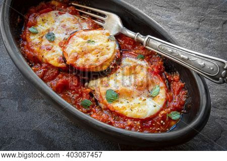 Baked eggplant or aubergine, with tomato and mozzarella, in black dish over slate.