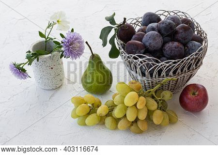 Just Picked Ripe Plums In Wicker Basket, An Apple, A Pear And A Bunch Of Ripe White Grapes On The Wh