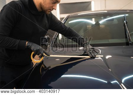 Auto Detailing Worker Pasting Protective Tape On The Car Hood Before Polishing. Car Body Preparation