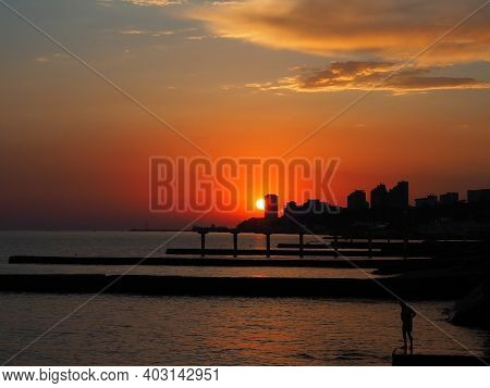 The Sun Sets Over The Sea And The City In The Bright Sunset Sky