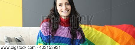 Smiling Woman Sitting On Sofa With Lgbt Flag. Female Homosexuality And Recognition Concept