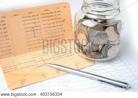 Pen On Account Book Bank With Coins In Glass Jar; Banking, Investment, Economy, Business Concept.
