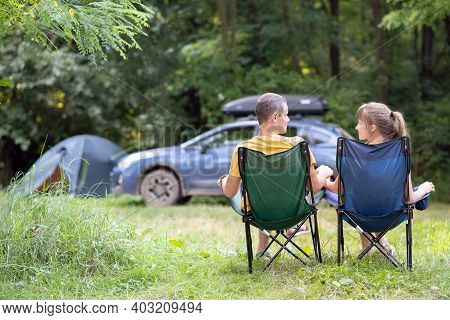 Back View Of A Happy Couple Sitting On Chairs At Campsite Relaxing Together. Travel, Camping And Vac