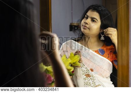 A Beautiful Indian Woman In White Saree Wearing Silver Earrings In Front Of Mirror With Smiling Face