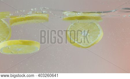 Close Up Of Falling Lemon Slices Into Splashing Water. Action. Fresh Citrus Fruit Slices Falling Dow