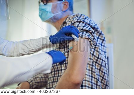 Young Woman Nurse With Surgical Mask And Face Shild Giving Injection To Senior Man. Covid-19 Or Coro