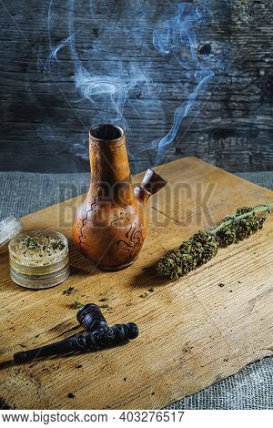 Old Brown Steamung Bong And Open Cannabis Grinder With Chopped Marijuana Weed And Medical Cannabis I