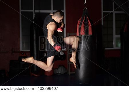 Kickboxing Fighter Performing Jumping Air Kicks With Knee On Punch Bag. Caucasian Man Practicing Mar