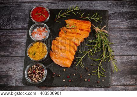 Chicken Fillet Thinly Sliced On A Black Ceramic Plate With Cooking Spices, Chili And Rosemary. Top V