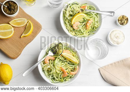 Delicious Zucchini Pasta With Shrimps And Lemon Served On White Wooden Table, Flat Lay