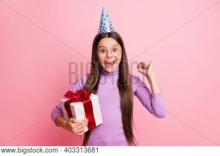 Photo Of Delighted Little Kid Girl Hold Gift Box Raise Fists Wear Purple Brithday Cone Isolated On P