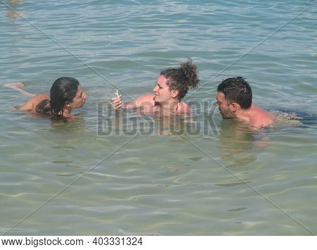 Young Beautiful Woman And Man Lying In Water In Sea While Sunbathing. Couple Of Tourists Are Bathing