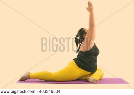 Studio Shot Of Young Fat Asian Woman Stretching Her Legs And Reaching Up While Doing Yoga Poses