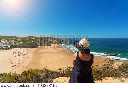 A Woman With A Hat On Her Head, On The Shore, Admires The View Of The Portuguese Beach, Odeceixe.