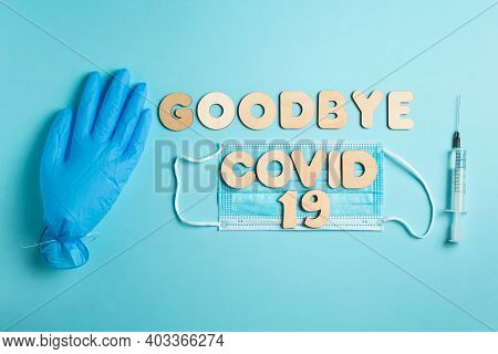 Words Goodbye Covid 19 From Wooden Letters And Syringe With Vaccine On A Blue Background, Inflated M