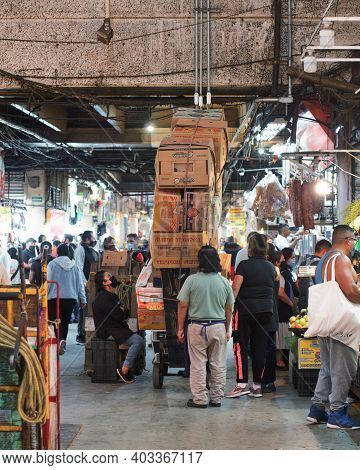 Crowd of people standing around stack of carton boxes in passage of wholesale market on Central de Abastos of Mexico City during coronavirus pandemic, Mexico, in December 12, 2020