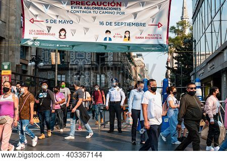 Crowd of ethnic people in masks walking past police officer with face shield under banner on street of Mexico City during coronavirus lockdown, Mexico, December 12, 2020