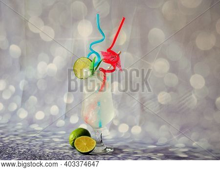 Glass Of Clear Citrus Juice With Ice And A Slice Of Lime, On A Gray Abstract Background.