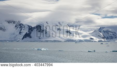 Antarctic Coastline With Snow Capped Mountains And Low Clouds