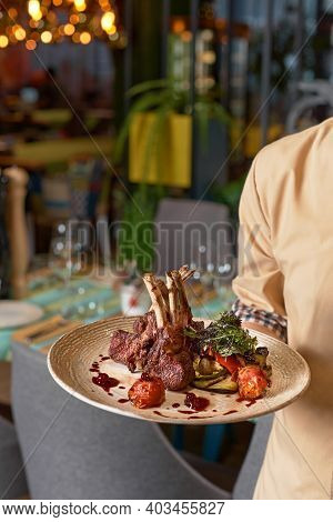Hands Holding Cooked Tomahawk Long Bone Ribeye Steak On A Plate In Restaurant At The Waitress's Hand