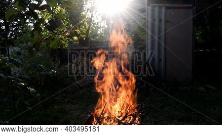 Defocus Bright Red Flame Of Bonfire Burning Outdoor With Flare Sunbeams From Sunset Sun. Rural Lands