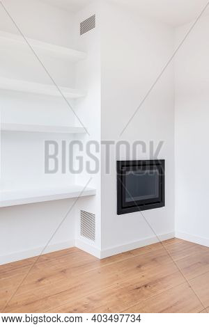 Part Of White Living Room In A Newly Renovated Apartment With A Fireplace, Shelves And Vents