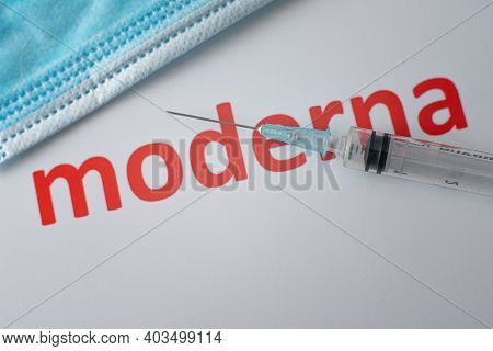 Red Moderna Sign An A Syringe And A Blue Face Mask On White Background, Denmark, January 15, 2021