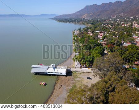 Side Aerial View Of Ajijic Boardwalk, Lake, And Some Trees. Lighthouse And Montains