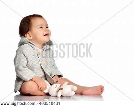 Baby And Toy Bunny Isolated. Barefoot Infant Child In Knitted Wear Sitting On White Floor Studio Bac