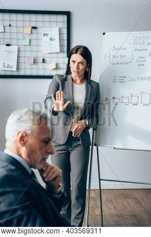 Worried Businesswoman Showing Stop Near Flipchart And Mature Investor On Blurred Foreground
