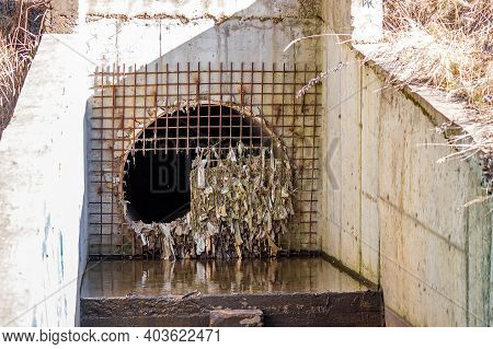 Storm Sewer Pipe Closed With Grating. Broken Sewer Entrance. Plastic Debris Stuck On The Drain Grate
