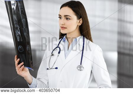 Professional Young Woman-doctor Is Looking At Her Patients Roentgenogram. Physician At Work In A Cli