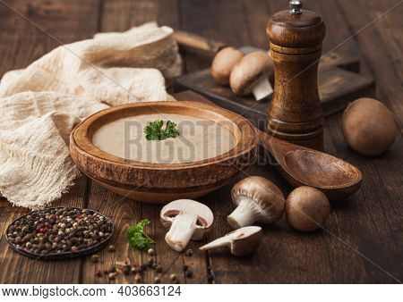 Wooden Plate Of Creamy Chestnut Champignon Mushroom Soup With Wooden Spoon, Pepper And Kitchen Cloth