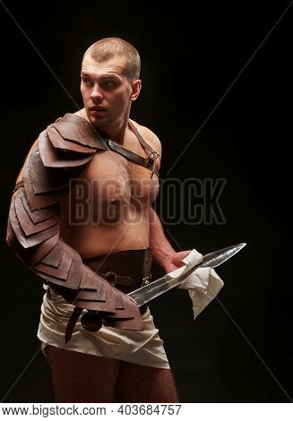 Gladiator With Sword And Armor On A Black Background. A Warrior In Gladiatorial Armor With A Sword I