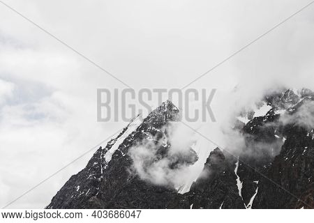Atmospheric Minimalist Alpine Landscape With Hanging Glacier On Snowy Rocky Mountain Peak. Low Cloud