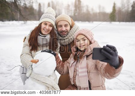 Portrait Of Happy Family Taking Selfie Photo Outdoors While Building Snowman Together And Enjoying W