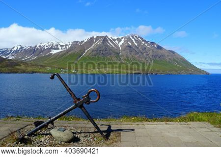 A Ship Anchor Overlooking The Mountain And Blue Fjord In The Summer Near Olafsfjordur, Iceland