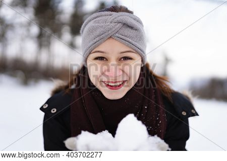 Happy young girl in winter clothes with snow looking in the camera and holding snowballs.