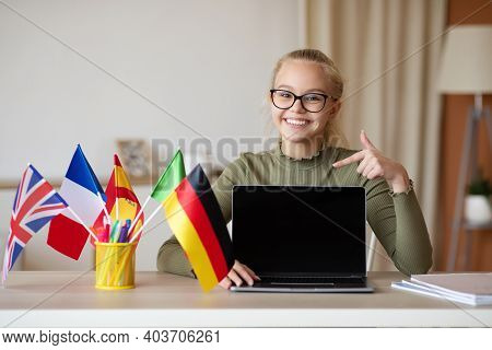 Happy School Girl Teenager With Glasses Pointing At Empty Laptop Screen, Sitting At Workdesk With Di