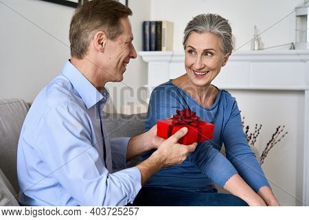 Happy Older Senior Couple Celebrating Valentines Day Sitting On Couch At Home. Loving Mature Husband