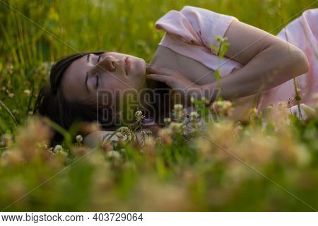 Portret Of A Girl With Dark Hair In A Pink Dress Lies And Sensually Touching Her Face In The Green G