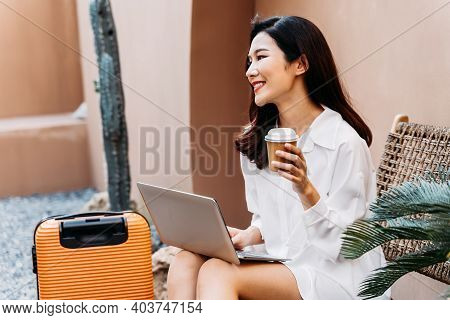 Young Asian Solo Traveling Woman With Smile Using Laptop And Drinking Coffee. Female Traveler Sittin
