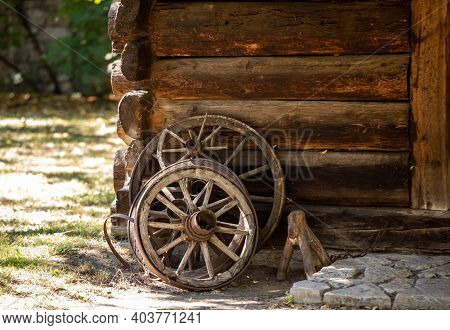 Wooden Wheels From An Ancient Cart Standing In Front Of The Wall Of A Wooden Country Cottage